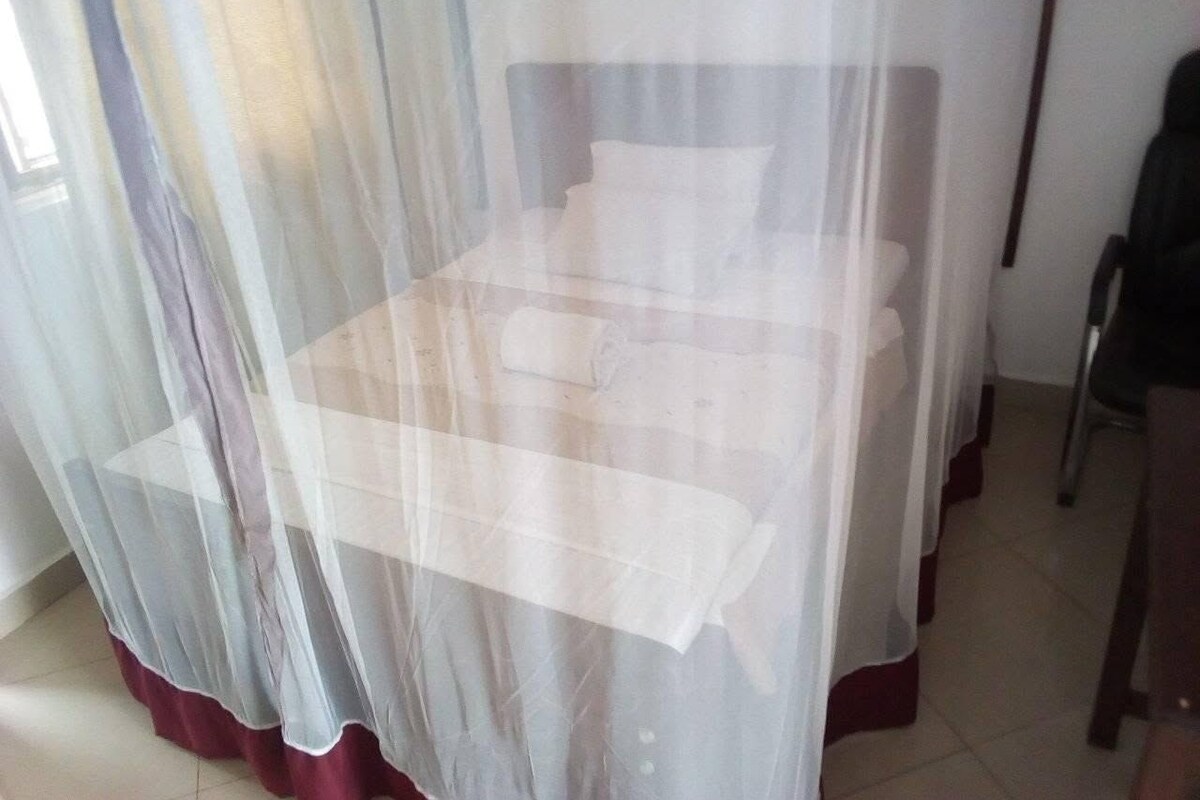 Una cama con cabecera blanca y una cortina translúcida.