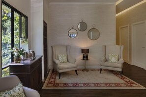 Una habitación con dos sillones, una mesita con lámpara y un muro decorativo con espejos.