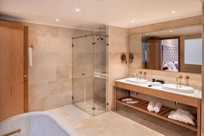 Un baño moderno con ducha envuelta en vidrio, tocador doble y una bañera grande.