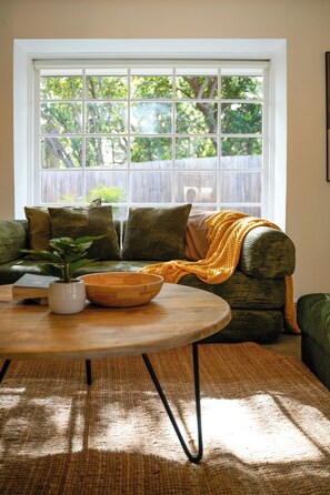 A cozy living room with a large window, a sofa with cushions, a coffee table with a bowl and a plant, and a woven rug. - Seednest Stylish 4BR Retreat Near Chadstone (Mount Waverley)