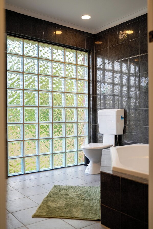 A modern bathroom with a toilet, a hand dryer, and a bathtub. - Seednest Stylish 4BR Retreat Near Chadstone (Mount Waverley)