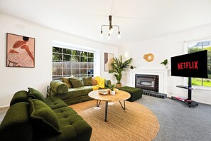 A living room with a green sofa set, a round coffee table, a fireplace, and a TV screen displaying 'NETFLIX'. - Seednest Stylish 4BR Retreat Near Chadstone (Mount Waverley)