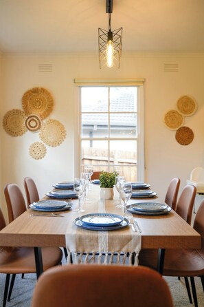 A dining area with a wooden table set for six, surrounded by chairs, with a hanging light fixture above. - Seednest Stylish 4BR Retreat Near Chadstone (Mount Waverley)