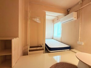 A compact room with a bed, a small table, a chair, a wall-mounted air conditioner, and a window with curtains. - Sunrise Voyage (Guangzhou)