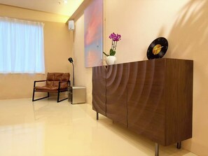 A modern room with a wooden cabinet, a leather chair, a vase with flowers, and a wall-mounted clock. - Sunrise Voyage (Guangzhou)