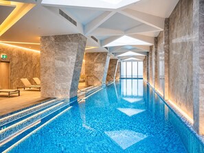 An indoor swimming pool with clear blue water, marble walls, and a modern ceiling design. - Central Melbourne 2BR - Pool, Gym & Free Trams (Melbourne)