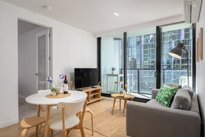 A modern living room with a TV, sofa, and dining area. - Central Melbourne 2BR - Pool, Gym & Free Trams (Melbourne)