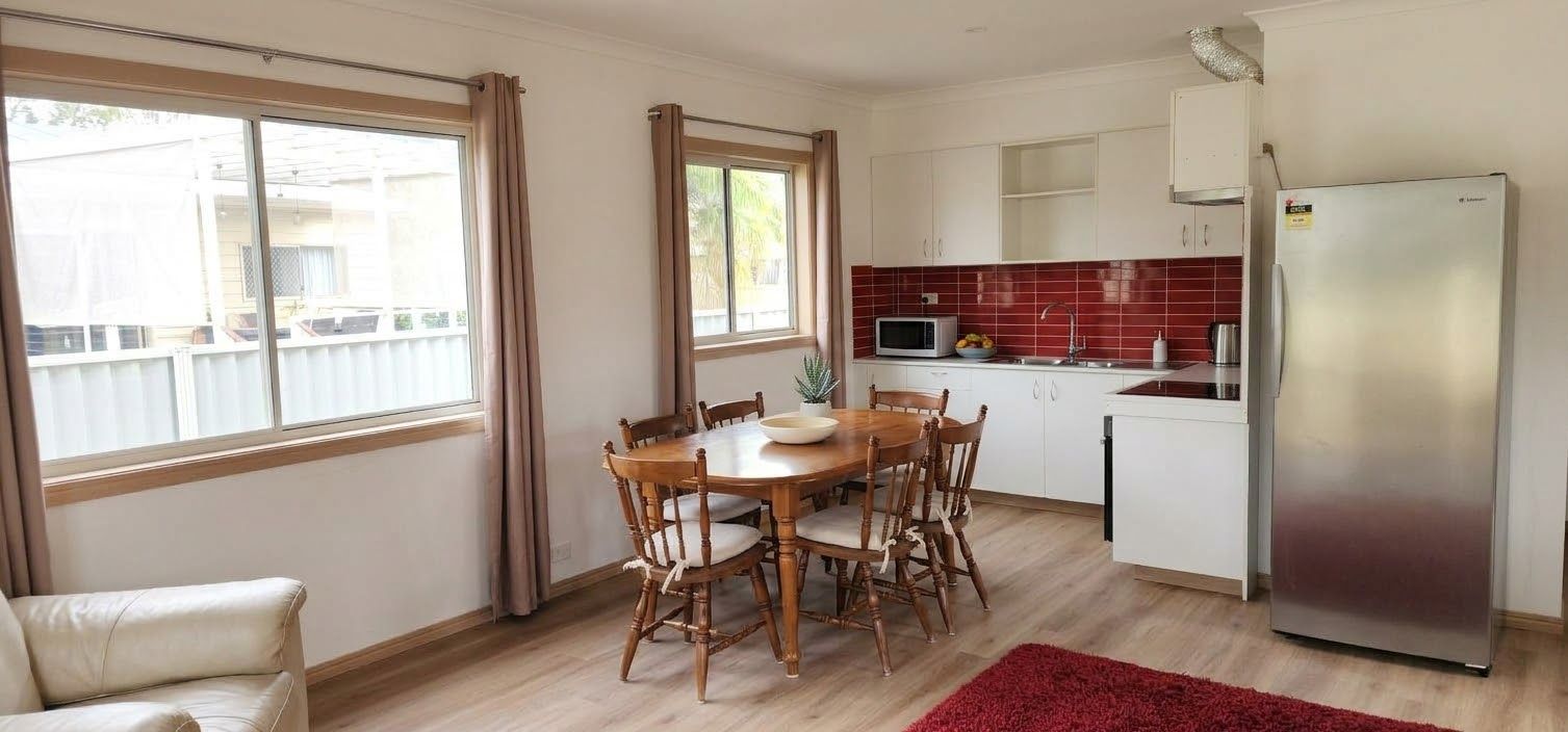 A compact kitchen with a dining table, chairs, a refrigerator, and a microwave.