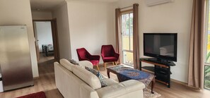 A living room with a sofa, two red chairs, a television on a stand, and a view through a window.