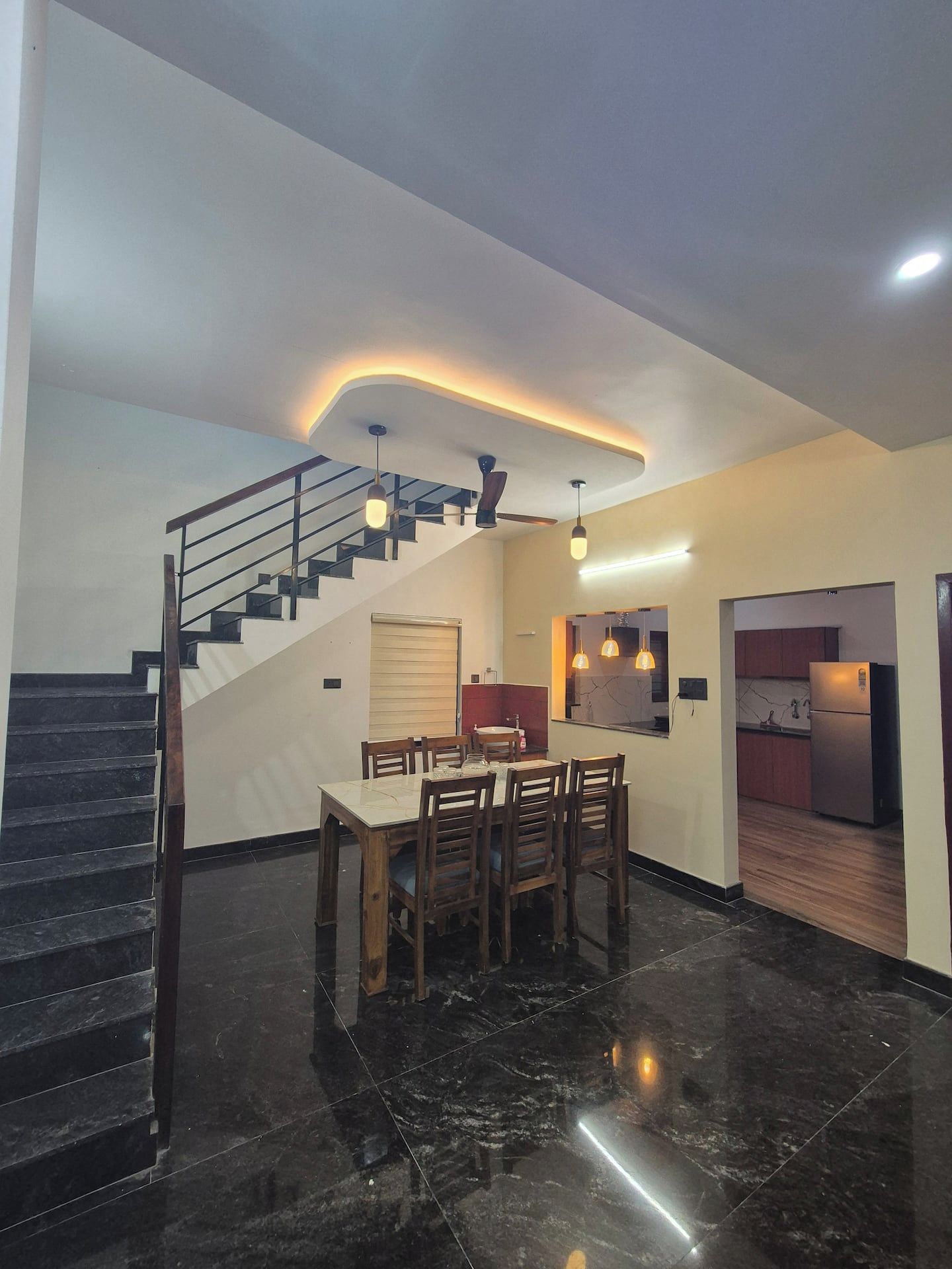 A modern interior with a staircase leading to an upper level, a dining area with a table and chairs, and a kitchen area with a refrigerator.