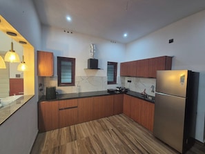 A modern kitchen with wooden cabinets, a stainless steel refrigerator, and a marble backsplash. - Serene Green Retreat Pothencode (Thiruvananthapuram)
