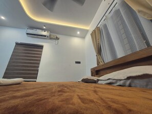 A bedroom with a bed, an air conditioning unit, a window with curtains, and a ceiling light fixture.