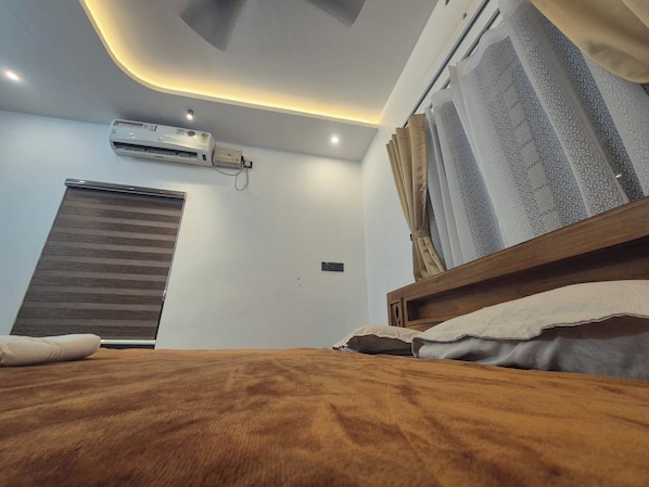 A bedroom with a bed, an air conditioning unit, a window with curtains, and a ceiling light fixture. - Serene Green Retreat Pothencode (Nedumangad)