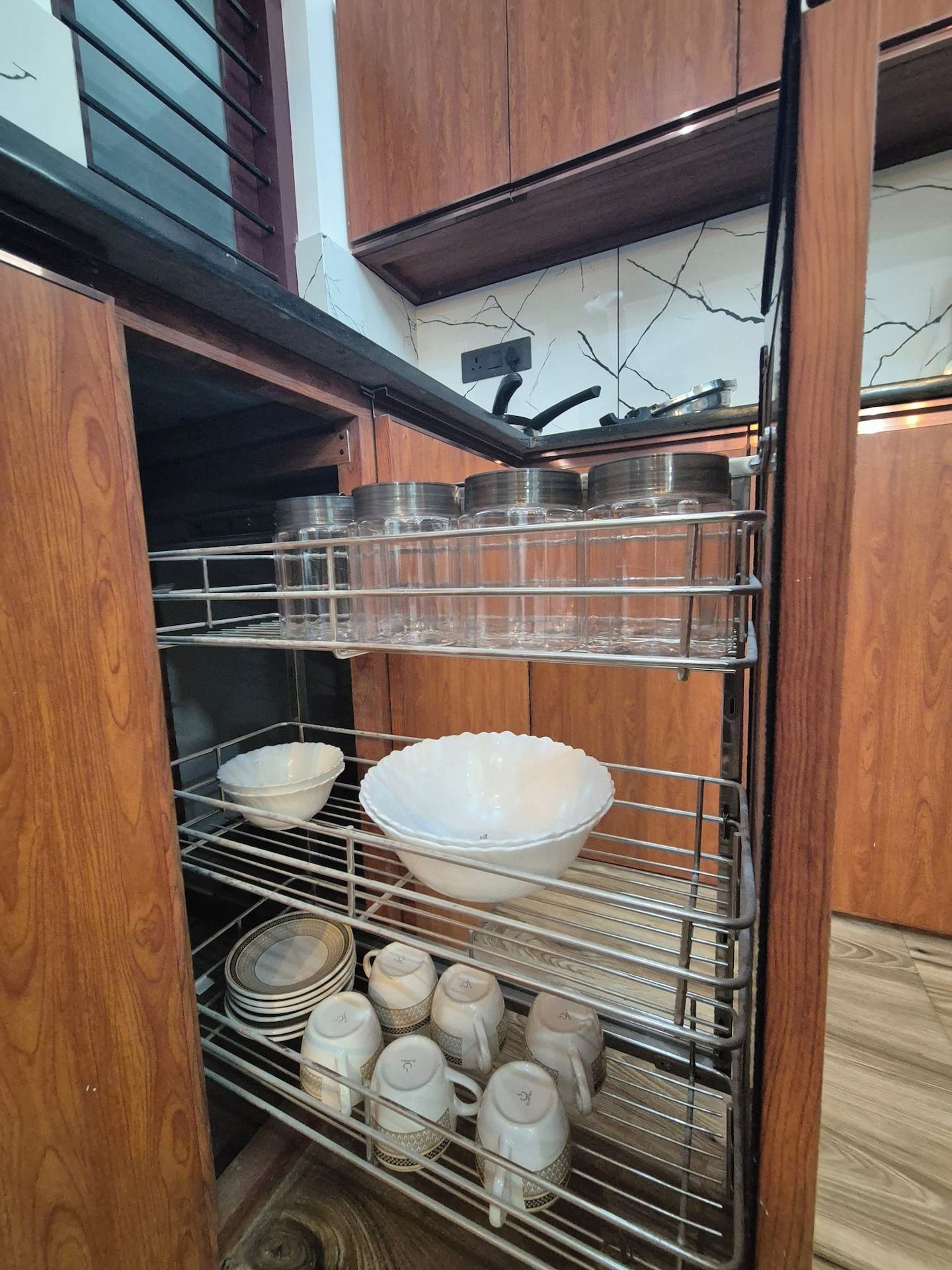 Una cocina con armarios de madera y una estantería metálica con platos y tazas.