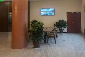 A lobby with a dining table, chairs, potted plants, a television, and a wooden door. - Gem Anqing Wangjiang County Central Mall Fengqi Road Hotel (Anqing)