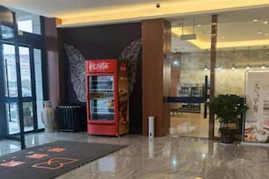 Un vestíbulo de hotel con un refrigerador de Coca-Cola, un mostrador de recepción y una planta en maceta.