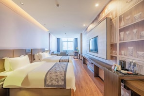 Habitación de hotel con dos camas, televisión, escritorio con cafetera y repisa con objetos decorativos.