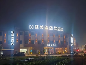 Un hotel con señalización iluminada, fachada moderna y zona de estacionamiento.