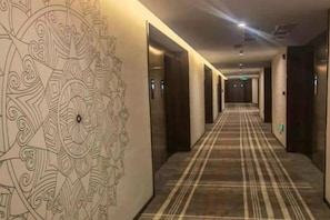 Un pasillo de hotel con detalles decorativos en la pared, piso alfombrado y puertas que dan a las habitaciones.