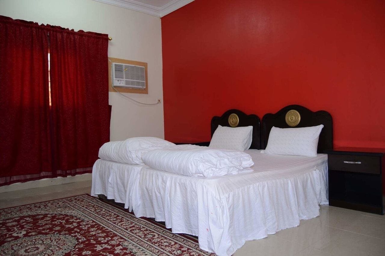 A bedroom with a double bed, a nightstand, a red wall, and a red curtain.