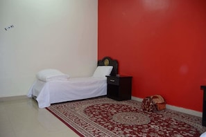 Un dormitorio con una cama, una mesita de noche, una pared roja y una alfombra estampada.