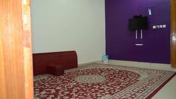 A room with a patterned carpet, a red sofa, a television mounted on a purple wall, and a wooden door.