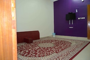 Una habitación con alfombra estampada, un sofá rojo, un televisor montado en una pared morada y una puerta de madera.
