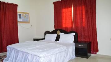A bedroom with a bed, nightstands, a red curtain, a wall-mounted air conditioner, and a red carpet.