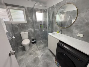 Un baño moderno con ducha de vidrio, inodoro, lavabo con espejo y lavadora.