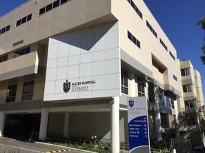 Un edificio moderno de hospital con un cartel que indica la entrada principal, Clínica Mater, estacionamiento y entregas.