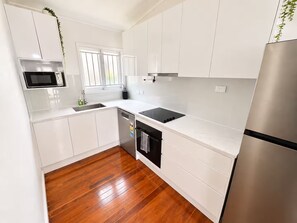 Una cocina moderna con armarios blancos, un refrigerador de acero inoxidable, un microondas, un lavavajillas y una ventana con persianas.
