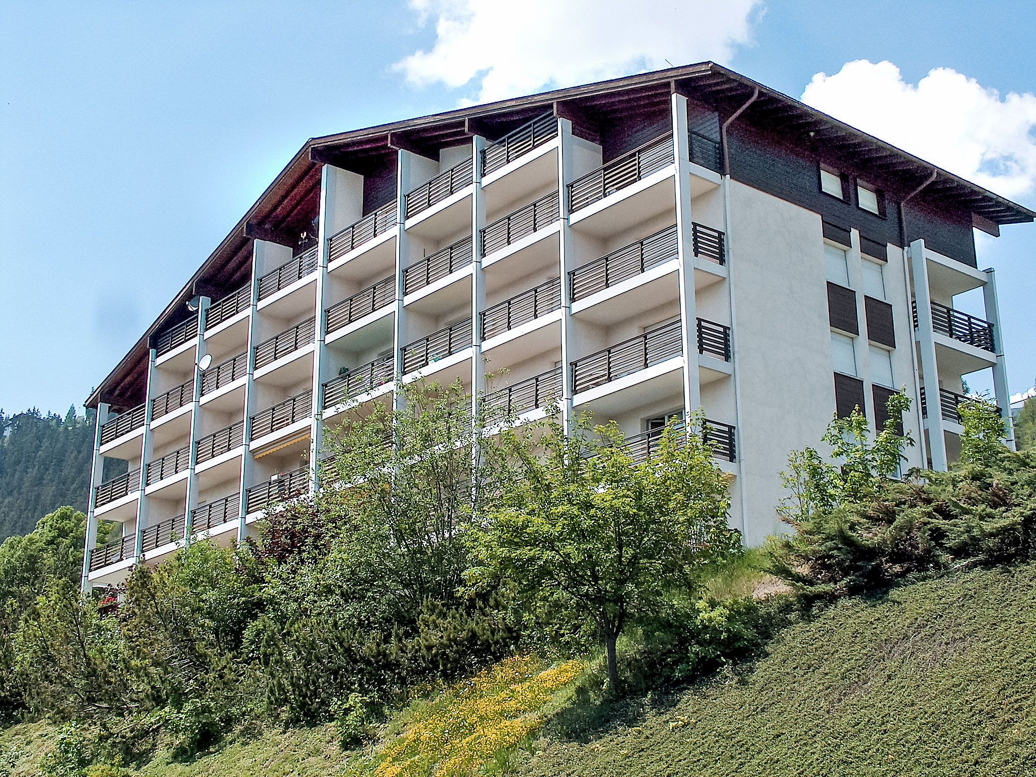 Un edificio de varios pisos con balcones, rodeado de vegetación y árboles.