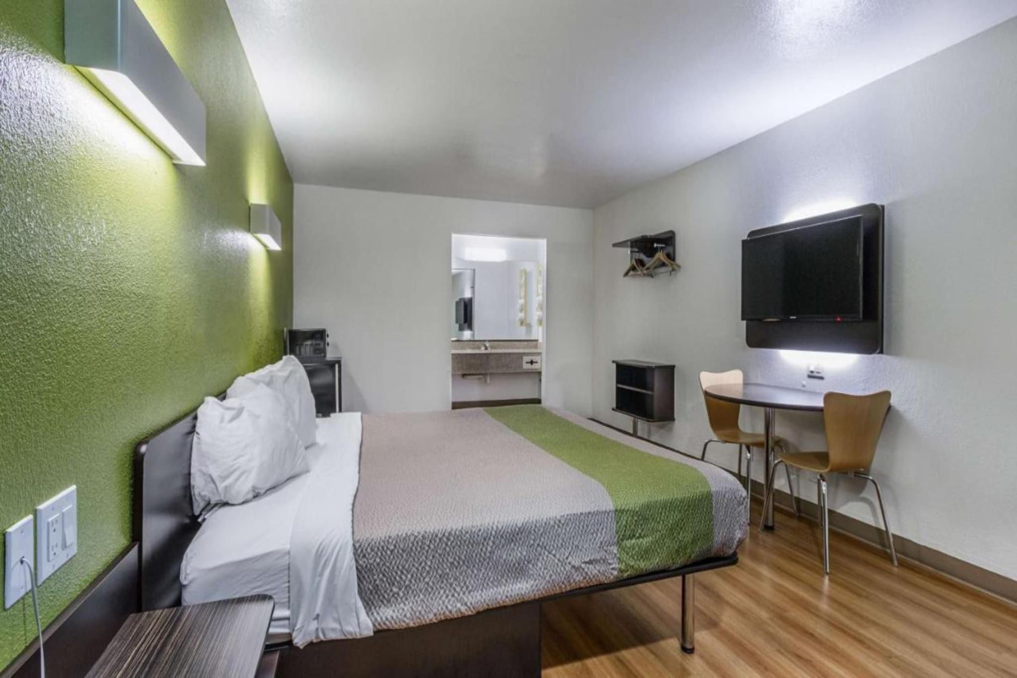 Ein Hotelzimmer mit Bett, Schreibtisch, Stuhl, Fernseher und Spiegel.