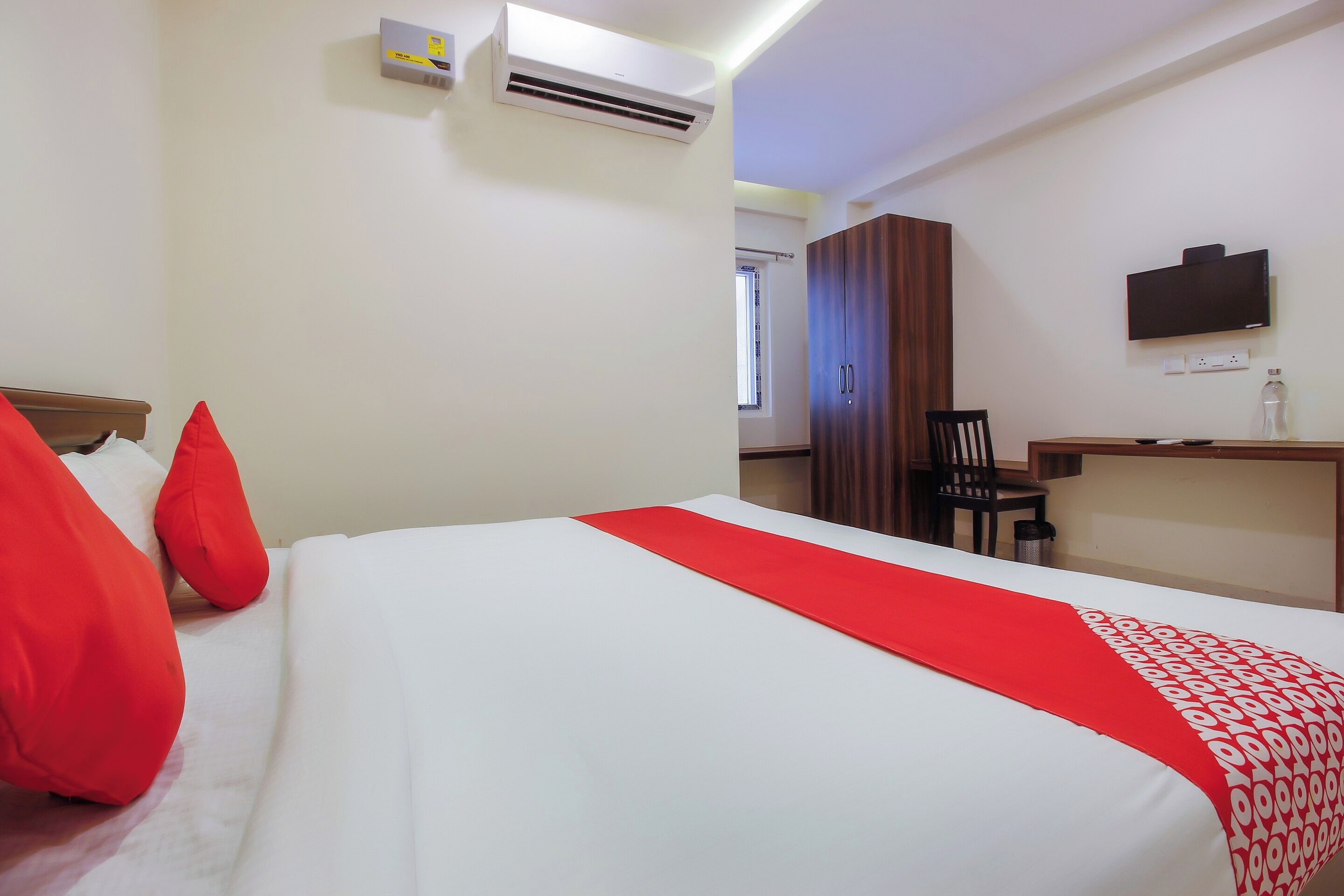 Quarto de hotel com cama, escrivaninha, cadeira, televisão e aparelho de ar condicionado.