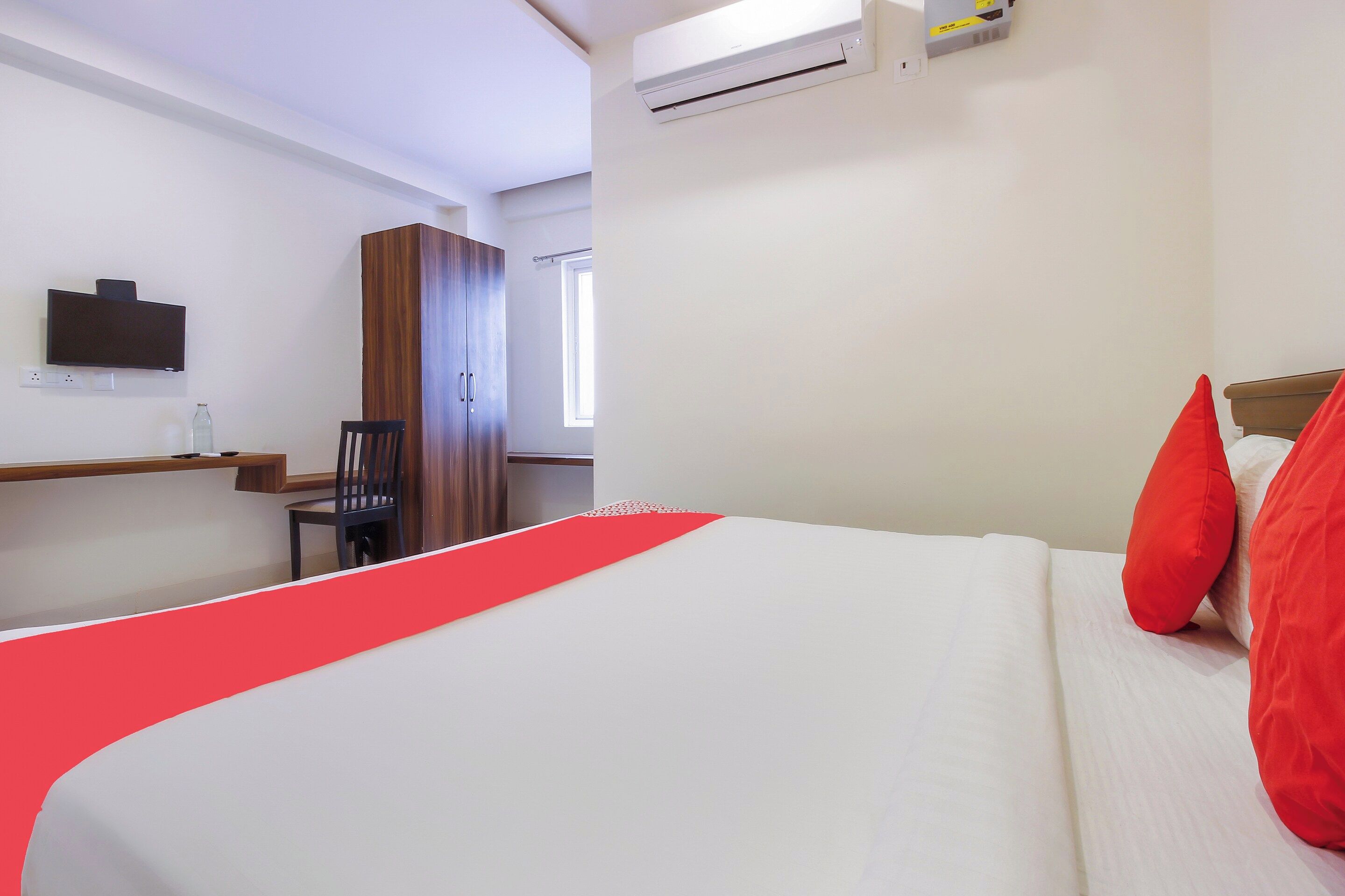 A hotel room with a bed, a TV mounted on the wall, a wardrobe, and a window.