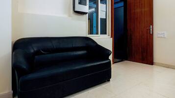 A room with a black sofa, a window, a wooden door, and a wall-mounted air conditioning unit.
