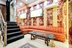 A lobby with a marble wall, a red leather sofa, a glass coffee table, and a staircase. - Hotel O Gold Wood (Amritsar)