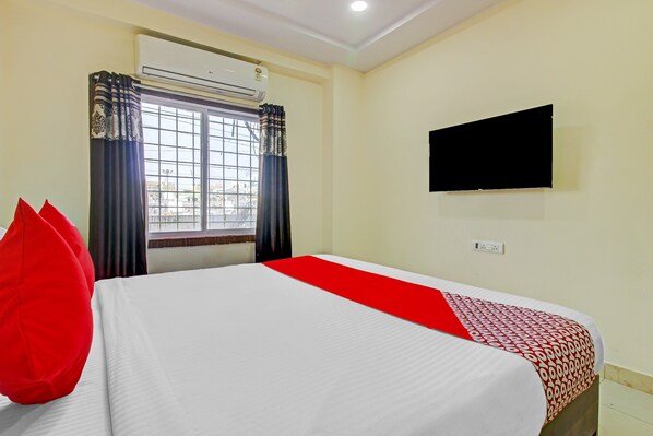 A hotel room with a bed, a TV mounted on the wall, and a window with curtains.