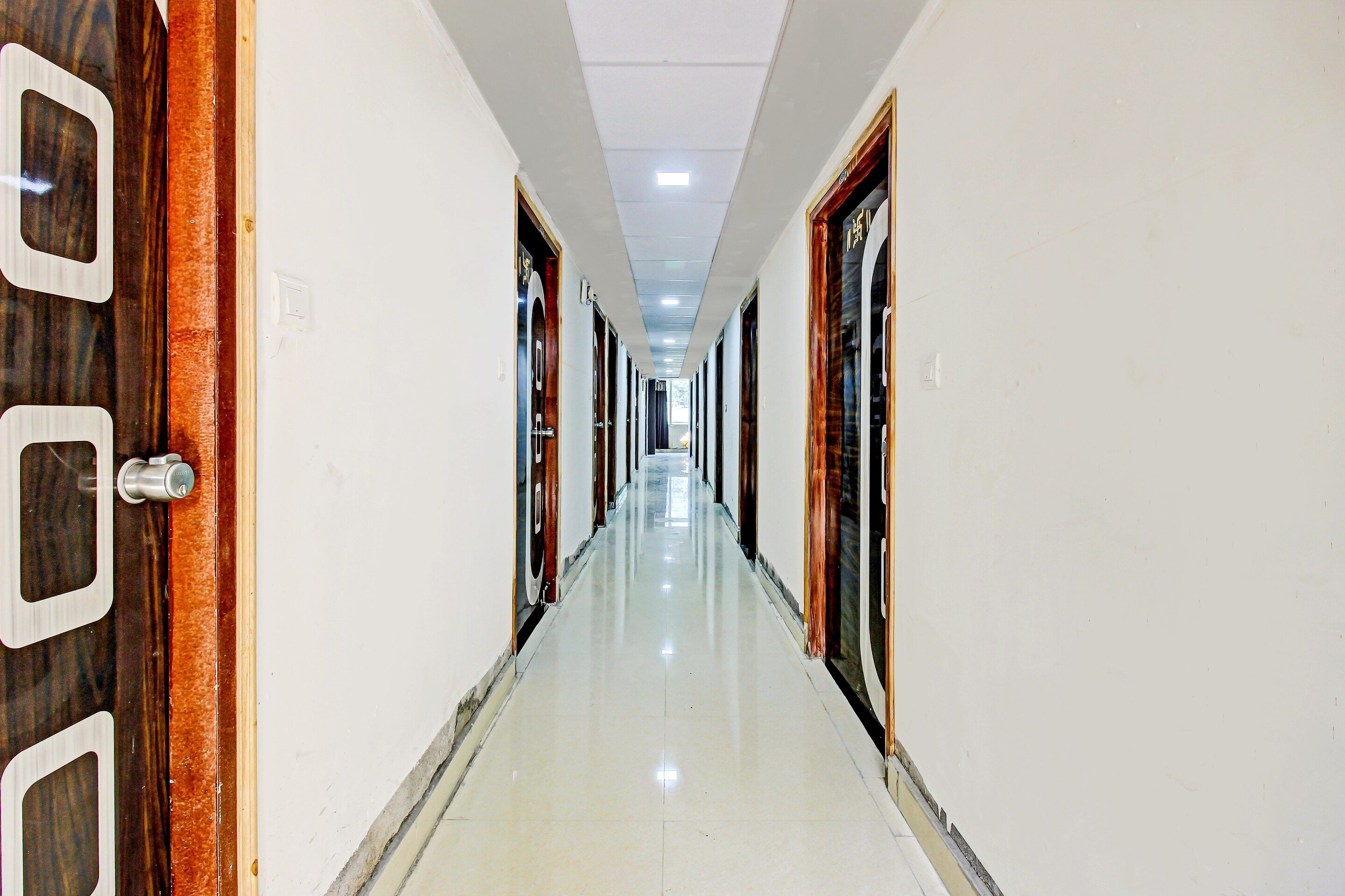 A long, narrow hotel corridor with doors on both sides, a tiled floor, and a ceiling with recessed lighting.