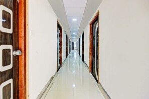 A long, narrow hotel corridor with doors on both sides, a tiled floor, and a ceiling with recessed lighting.