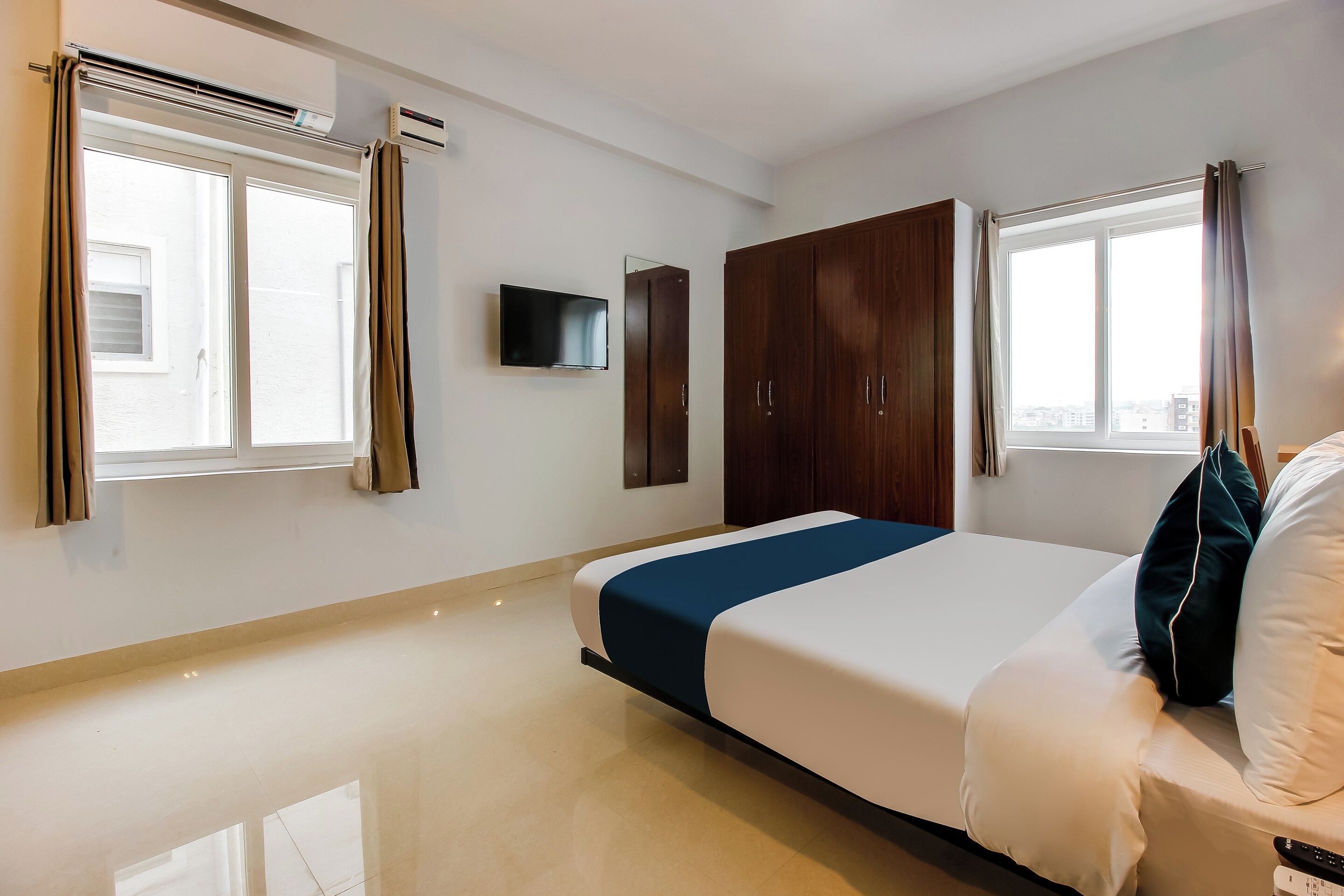 Habitación de hotel con cama, armario, televisor de pantalla plana y ventanas con cortinas.