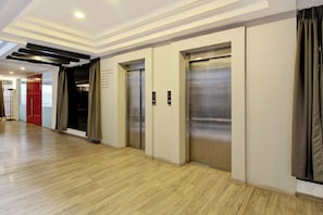Un pasillo con dos ascensores, piso de madera y una puerta roja.