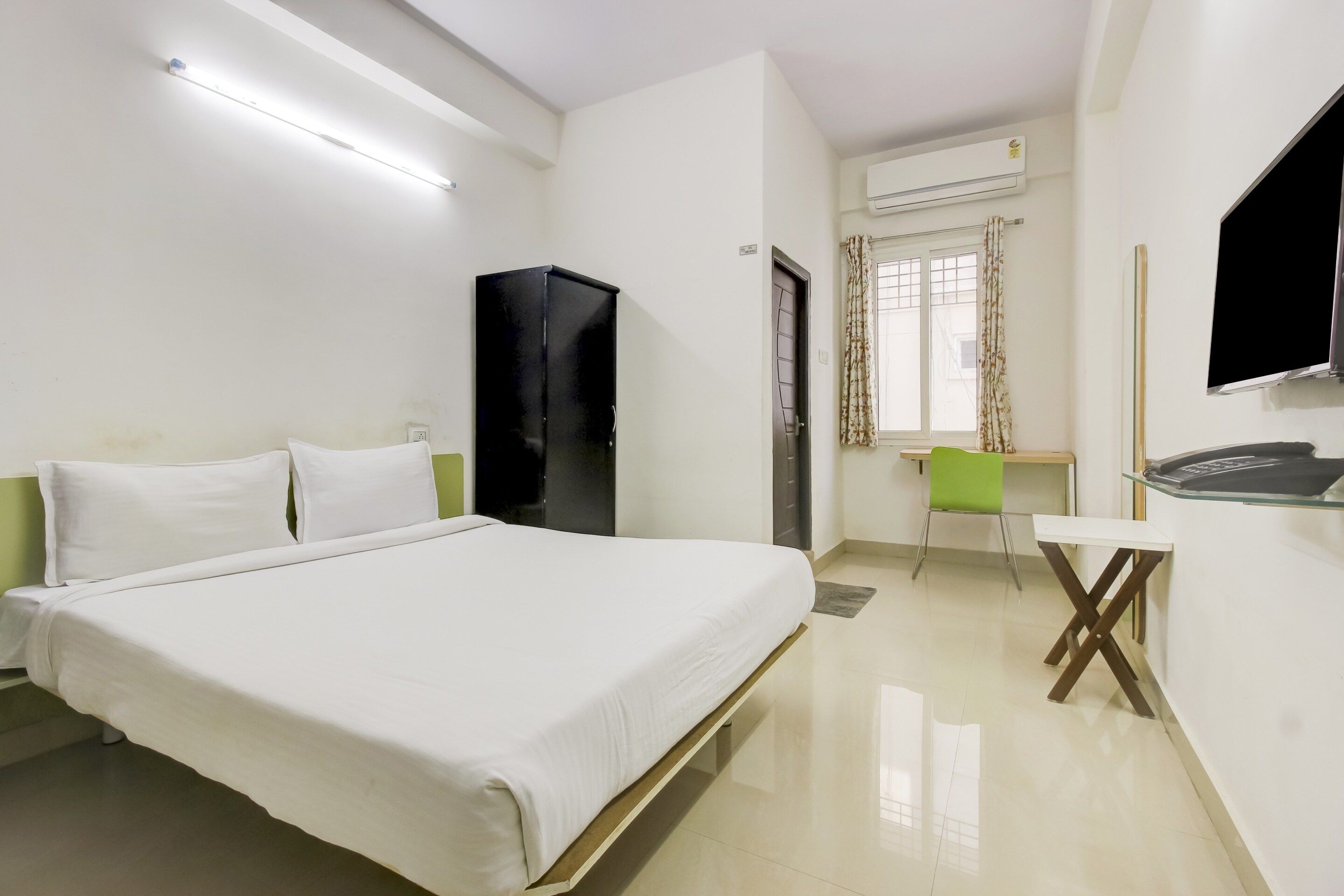 Habitación de hotel con cama, escritorio, silla, equipo de aire acondicionado y televisor.