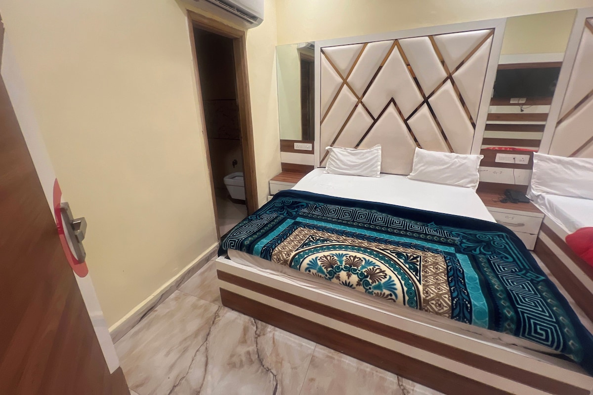 A hotel room with a bed, a bedside table, a mirror, and an air conditioning unit.