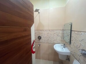 Un bany amb una porta de fusta, una dutxa, un lavabo amb mirall i rajoles amb motius florals.