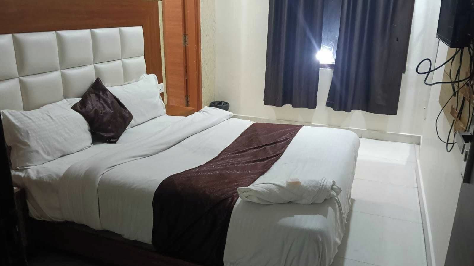 A bed with a headboard, a dark-colored throw blanket, and a white pillow.