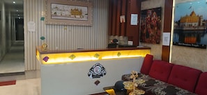A reception area with a reception desk, a seating area with a sofa, and a wall with framed pictures of temples. - Hotel O R D International (Amritsar)