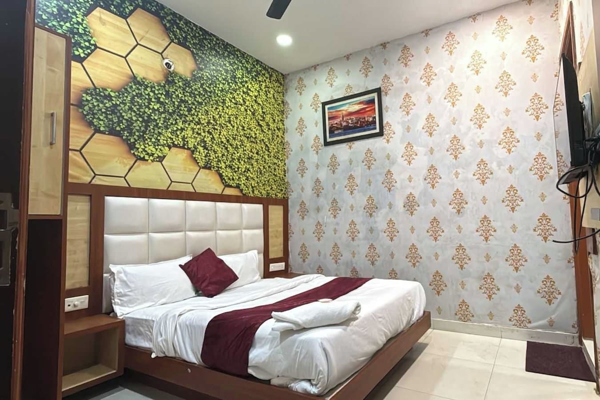 A hotel room with a bed, a headboard, a wall with a patterned wallpaper, a ceiling fan, and a framed picture on the wall.
