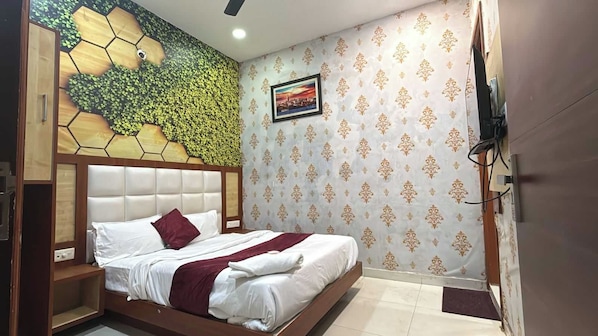 A hotel room with a bed, a headboard, a wall with a patterned wallpaper, a ceiling fan, and a framed picture on the wall. - Hotel O R D International (Amritsar)