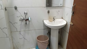A bathroom with a white sink, a mirror, and a shower with a faucet. There is a bucket on the floor. - Hotel O R D International (Amritsar)